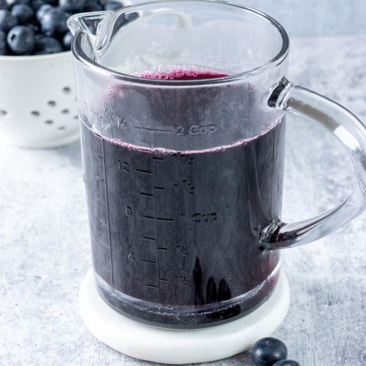 A jar of homemade blueberry syrup with a berry bowl filled with blueberries in the background.