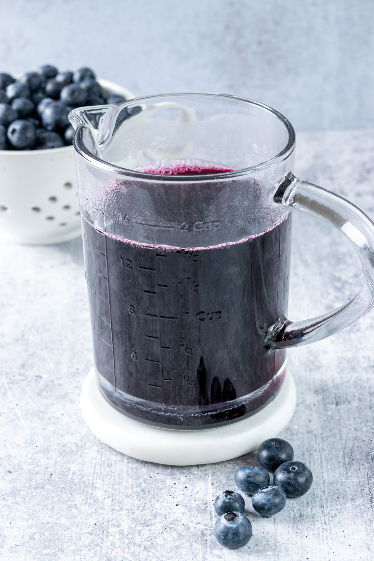 A jar of homemade blueberry syrup with a berry bowl filled with blueberries in the background.