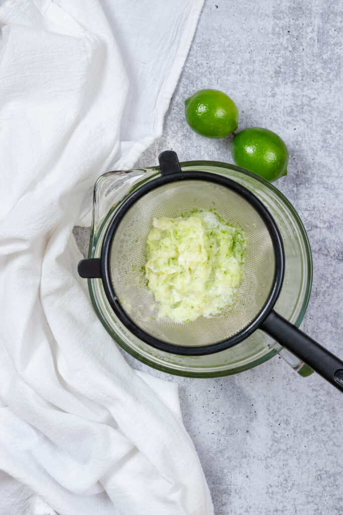 A strainer over a bowl full of the lime solids. The bowl has the strained lime juice in it.