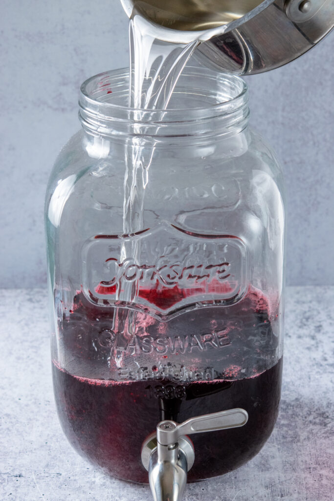 Pouring the homemade simple syrup into the hibiscus tea concentrate in a gallon container.