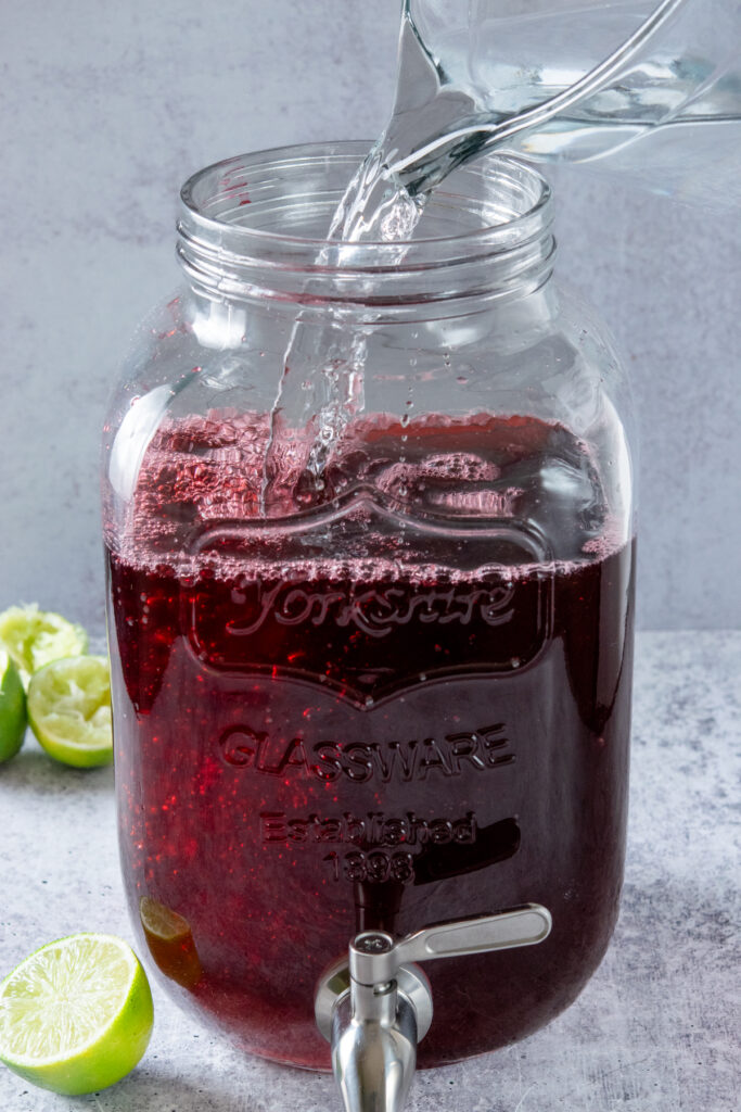 Adding cold water to the gallon of hibiscus iced tea.