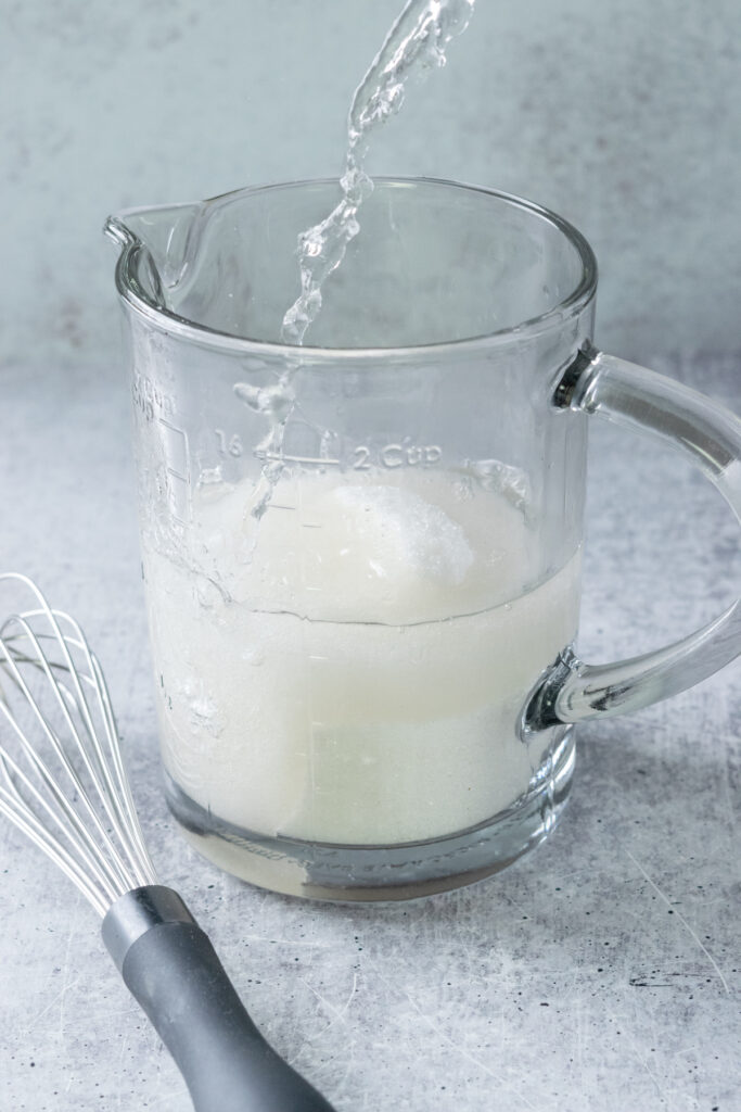 Making simple syrup for the lemonade by pouring boiling water into a glass measuring cup that has white sugar in it.