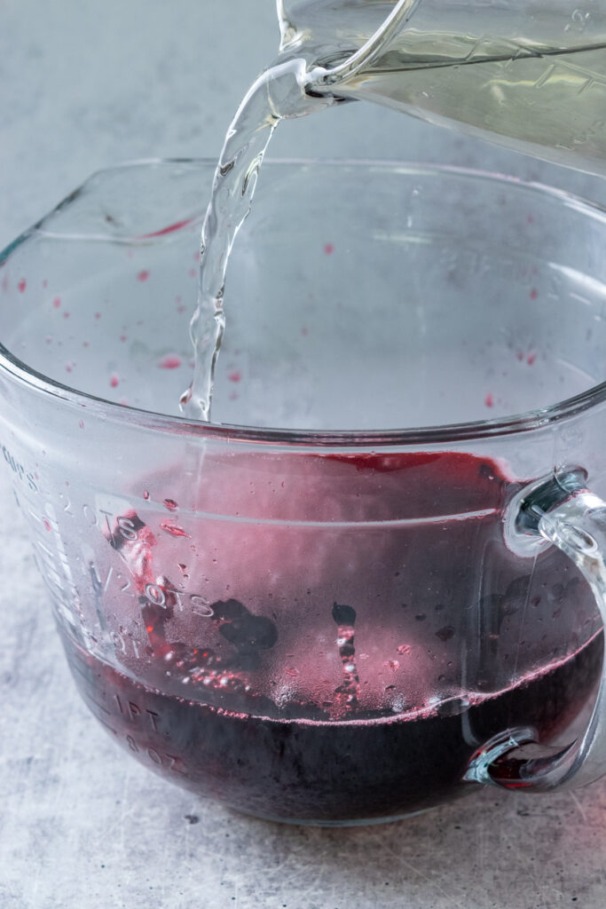 Pouring simple syrup into concentrated hibiscus tea to make homemade hibiscus lemonade.