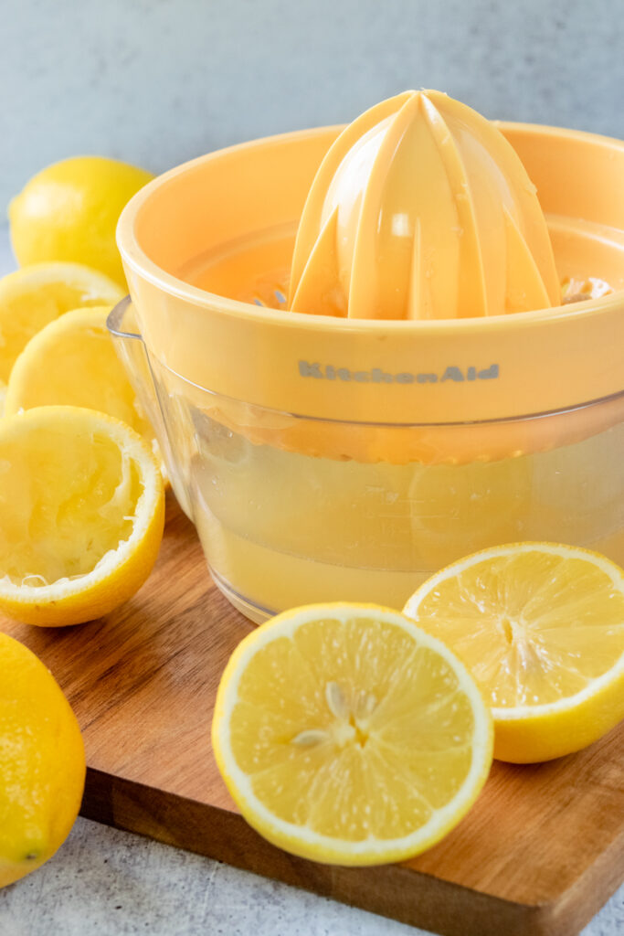 A yellow citrus juicer that has some freshly squeezed lemon juice in it. The juicer is surrounded by lemons that have already been juiced.
