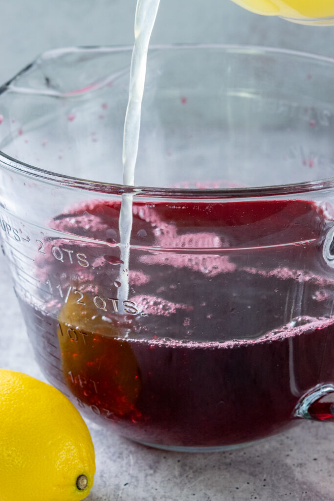 Pouring freshly squeezed lemon juice into concentrated hibiscus tea to make homemade hibiscus lemonade.
