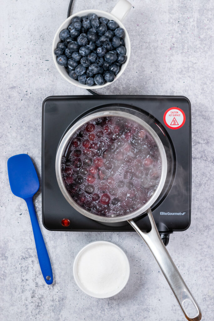 Blueberries and water in a saucepan on the stove. Steam is rising up from the saucepan.