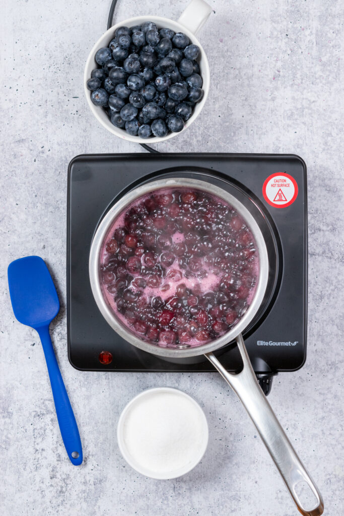 Cooking blueberries in water on the stove to make blueberry syrup. The berries are becoming a pink color as they cook.