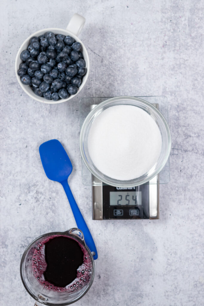 Weighing sugar on a kitchen scale to measure the amount needed to make the blueberry simple syrup.