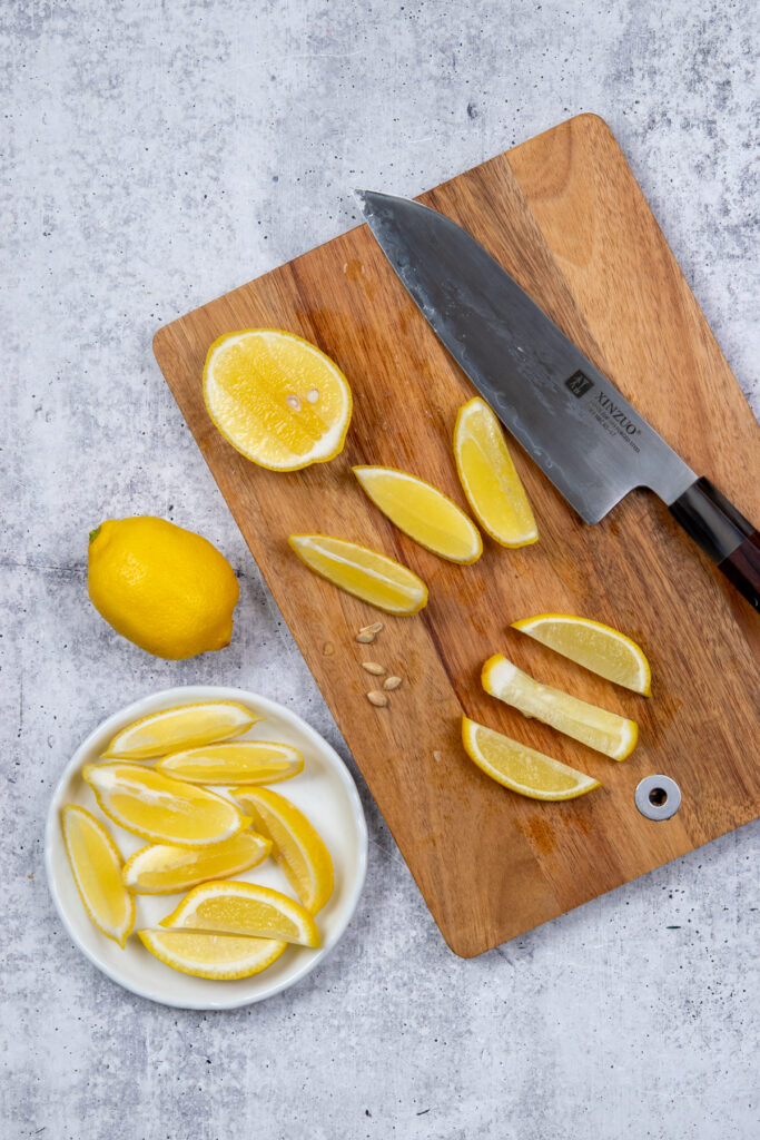 An overhead photo of a lemon being sliced on a cutting board.
