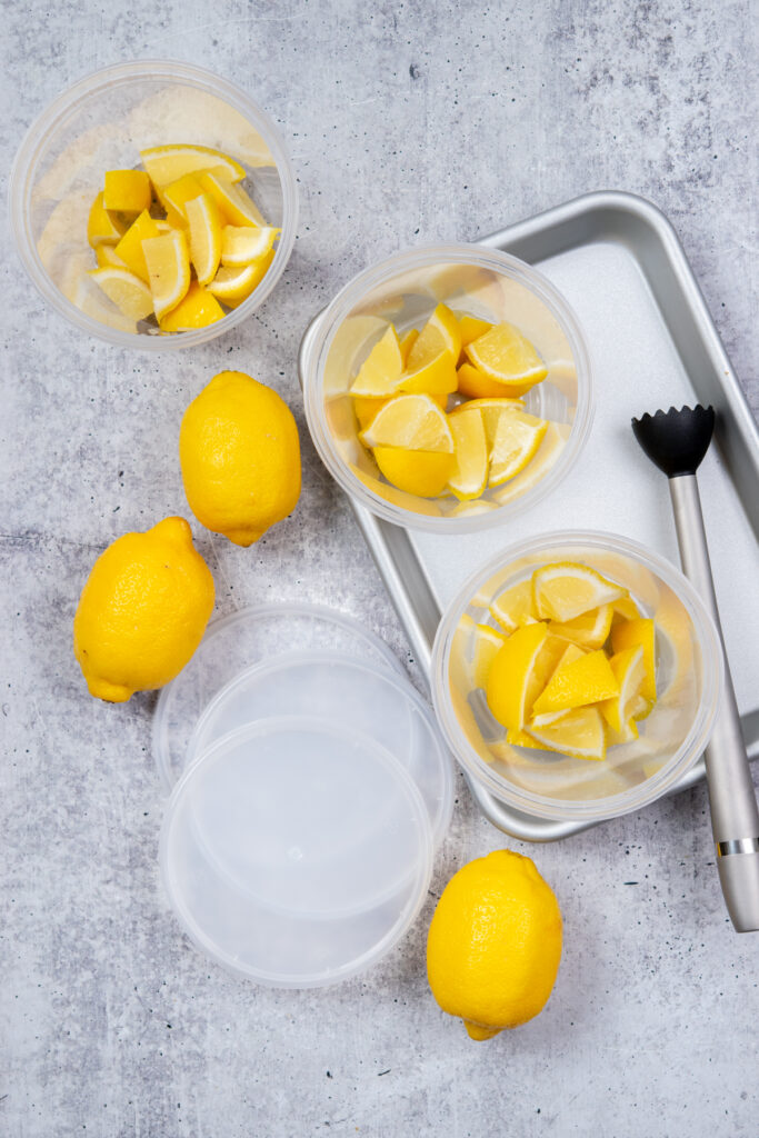 Overhead photo showing the steps to make state fair lemonade at home. There are three deli cups that have pieces of lemon in them. Next to the cups are the lids and a muddler.