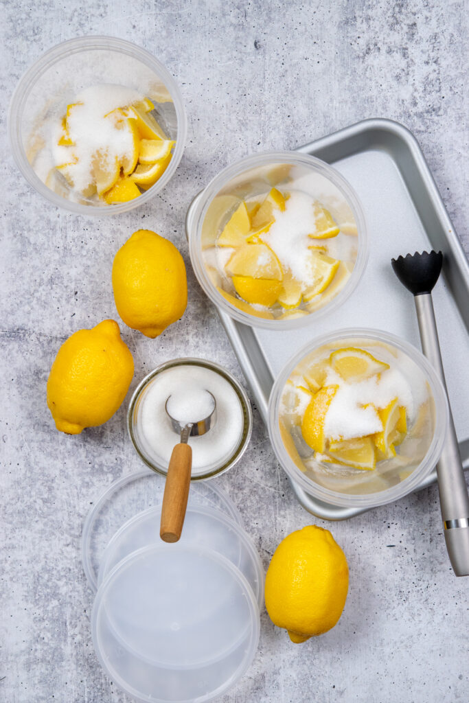 An overhead photo showing sugar added to cups with lemons to make state-fair style lemonade at home.