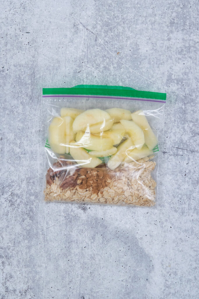 An apple smoothie freezer pack in a zip-loc-baggie. The pack has oats, pecans, cinnamon, salt and frozen apple slices in it.
