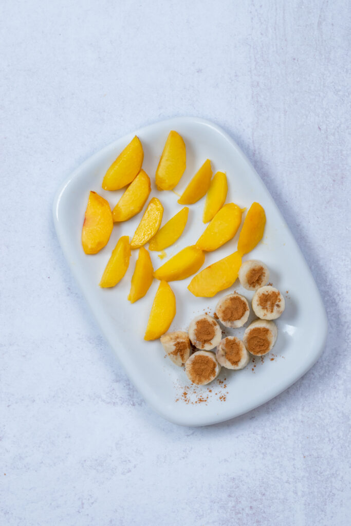 Baking sheet with peaches on one side and cinnamon-dusted banana chunks on the other—ready for the freezer.