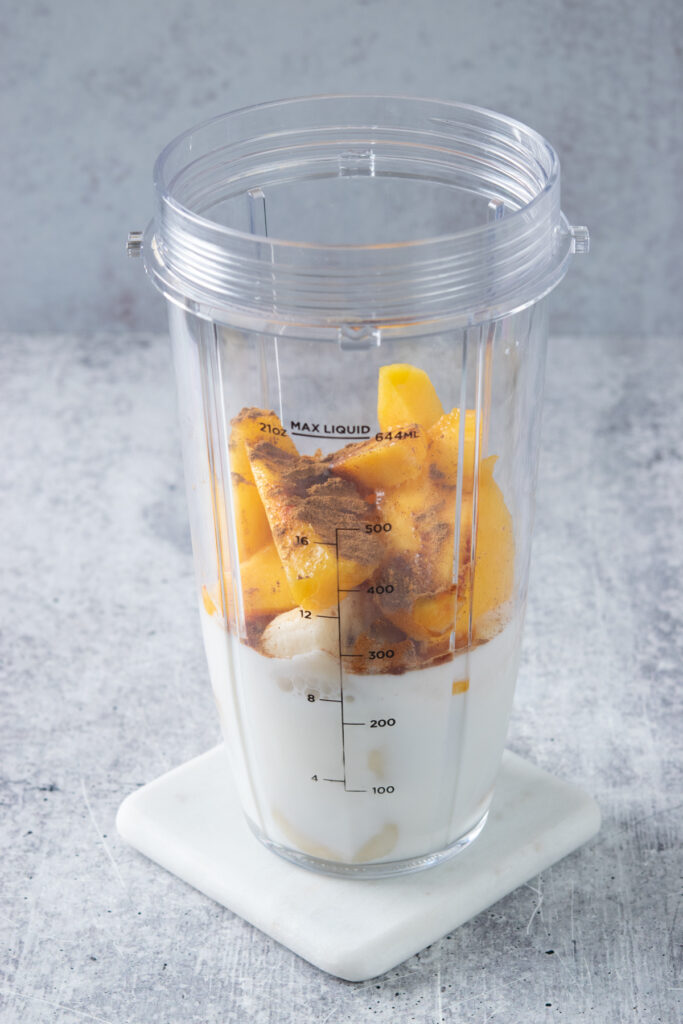 Ground cinnamon and vanilla added to the peaches, banana and milk in a blender cup.