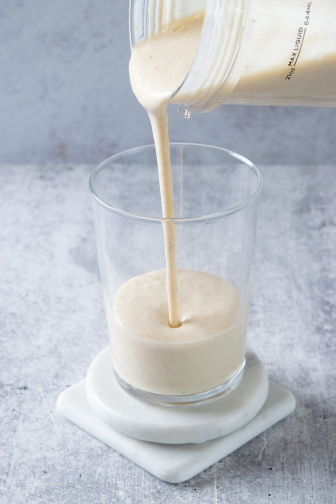 Pouring the peach banana smoothie from the blender cup into a glass.