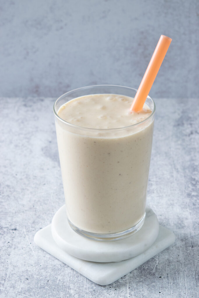 A super creamy peach banana smoothie in a glass that has an orange straw inserted into it.