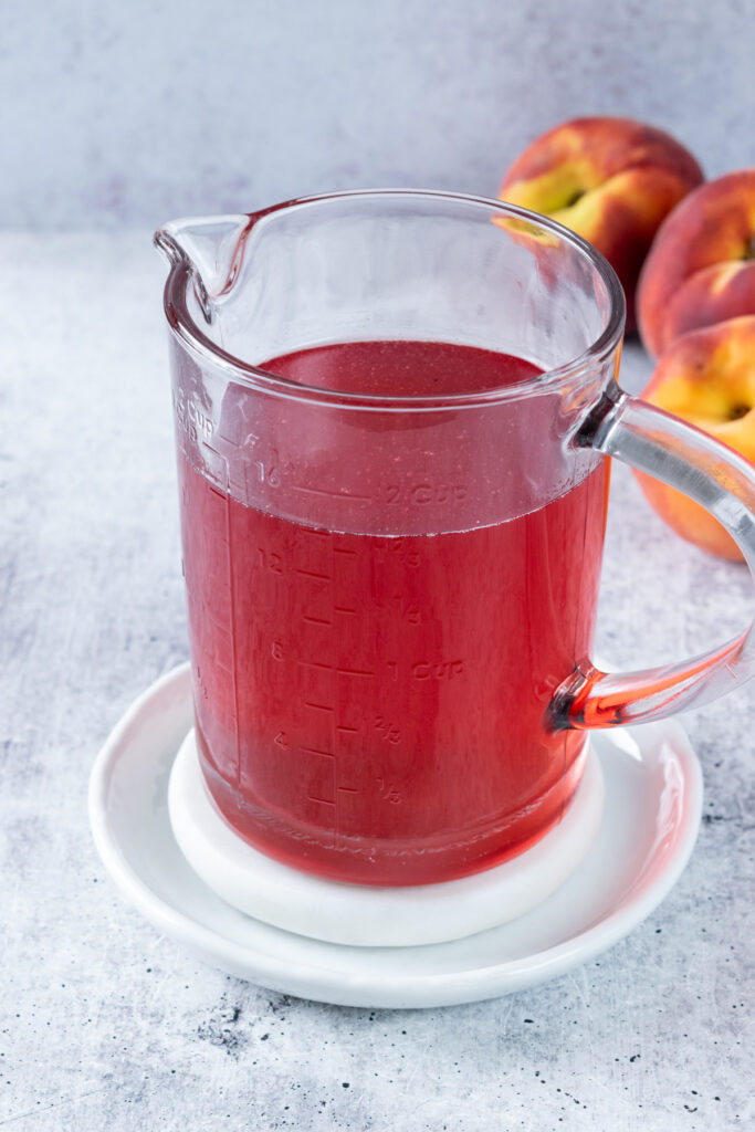 Container holding 1¾ cups of finished homemade peach syrup with a fresh peach beside it.