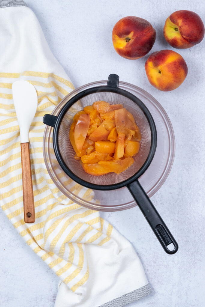 Peaches sitting in a fine mesh strainer over a bowl, ready for juice extraction.