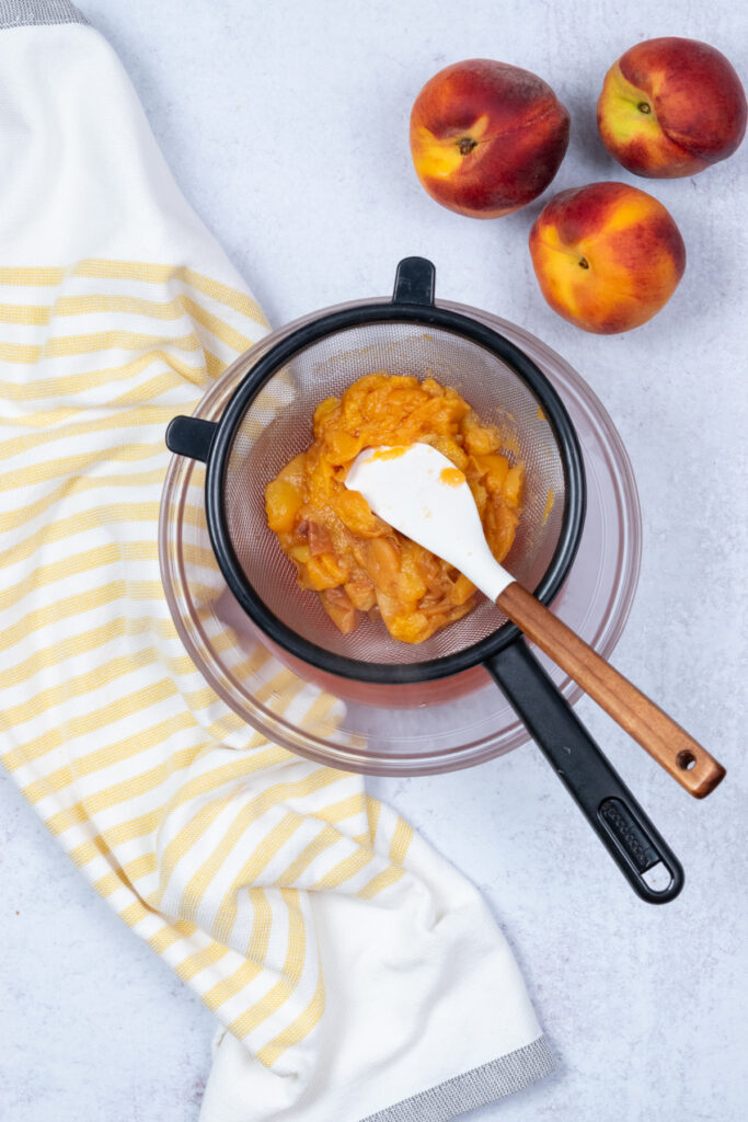 Pressing peaches in the strainer to extract as much juice as possible.