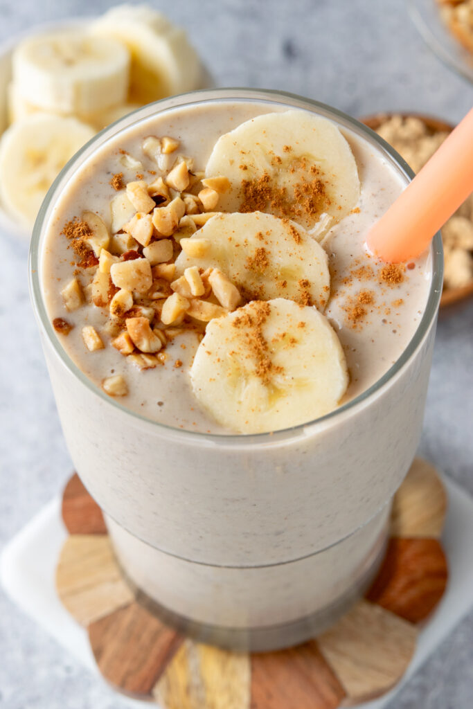 A protein-filled peanut butter banana smoothie that has crushed peanuts and banana slices on top with a sprinkle of cinnamon. The smoothie looks rich and creamy.