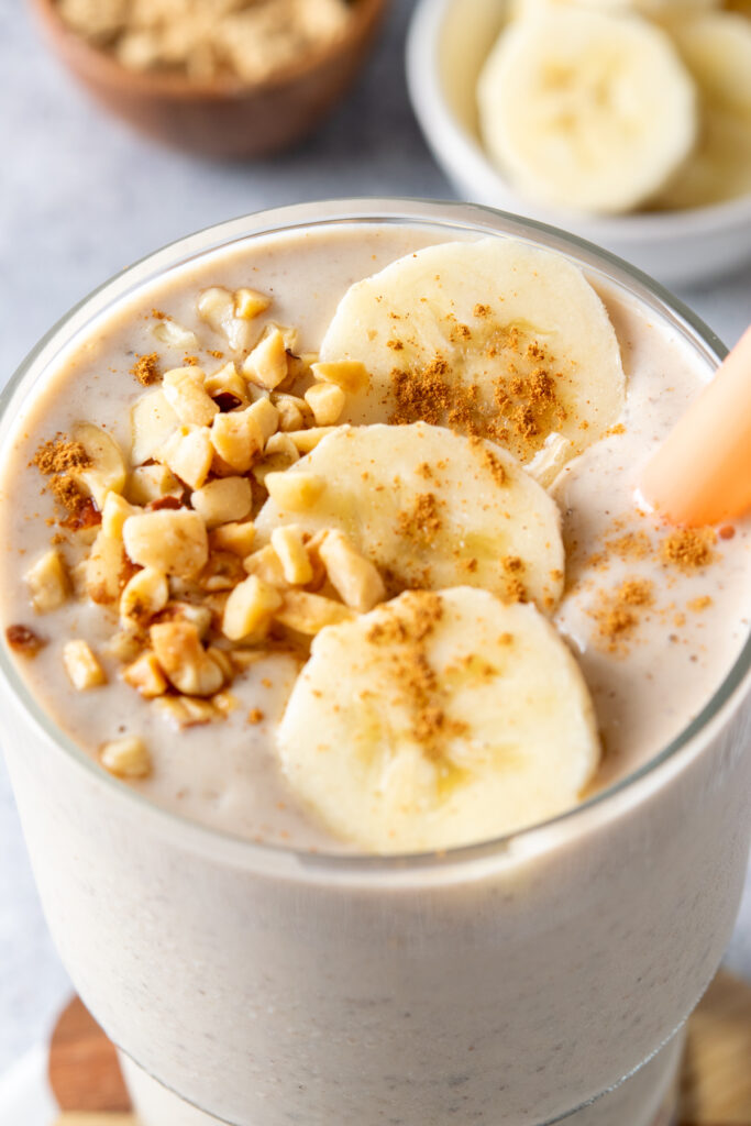 A close-up view of the top of a peanut butter banana smoothie. It has crushed peanuts, banana slices and cinnamon sprinkled on top of the thick and creamy smoothie.