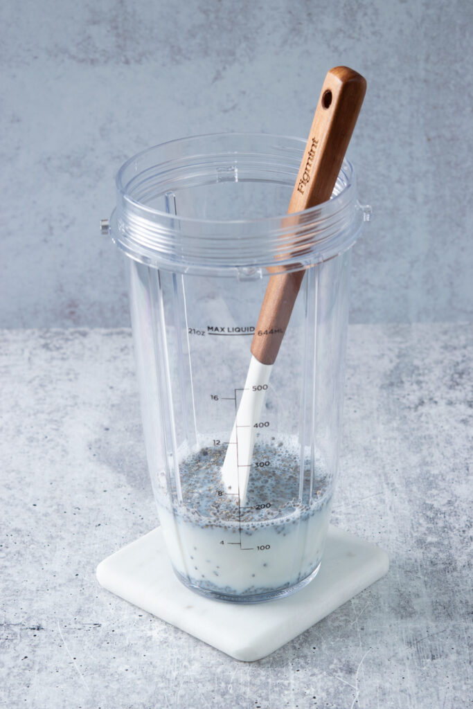 Milk and chia seeds added to blender cup to make a peanut butter banana smoothie.