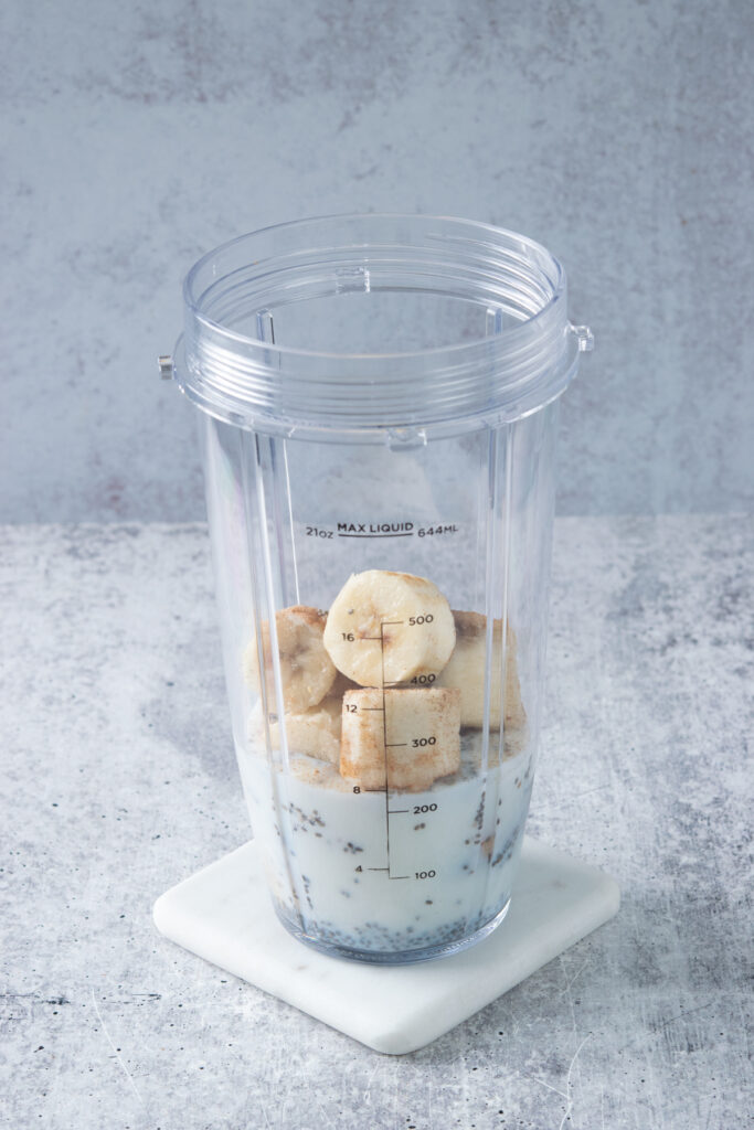 Frozen banana and cinnamon added to blender cup with milk and chia seeds.