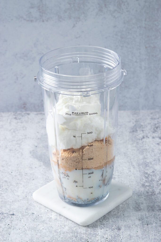 Greek yogurt in blender cup with all the other ingredients needed to make a peanut butter banana smoothie.