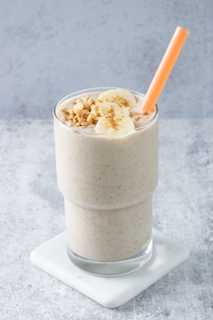 The smoothie has a straw in it and crushed peanuts and banana slices on top.