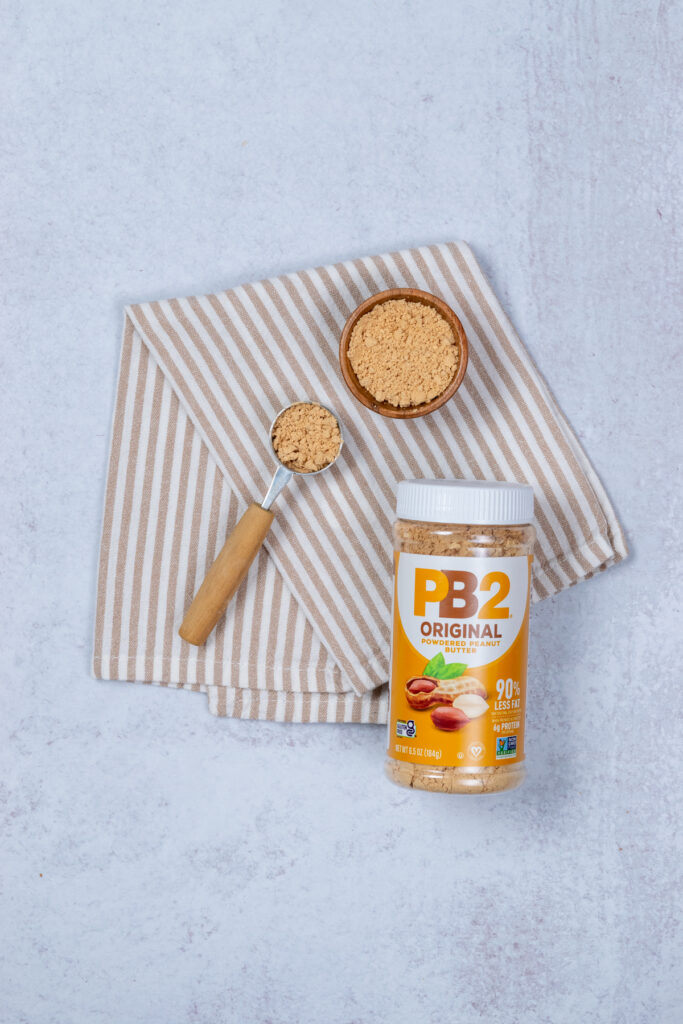 A jar of PB2 powdered peanut butter and some scooped out in a measuring spoon.