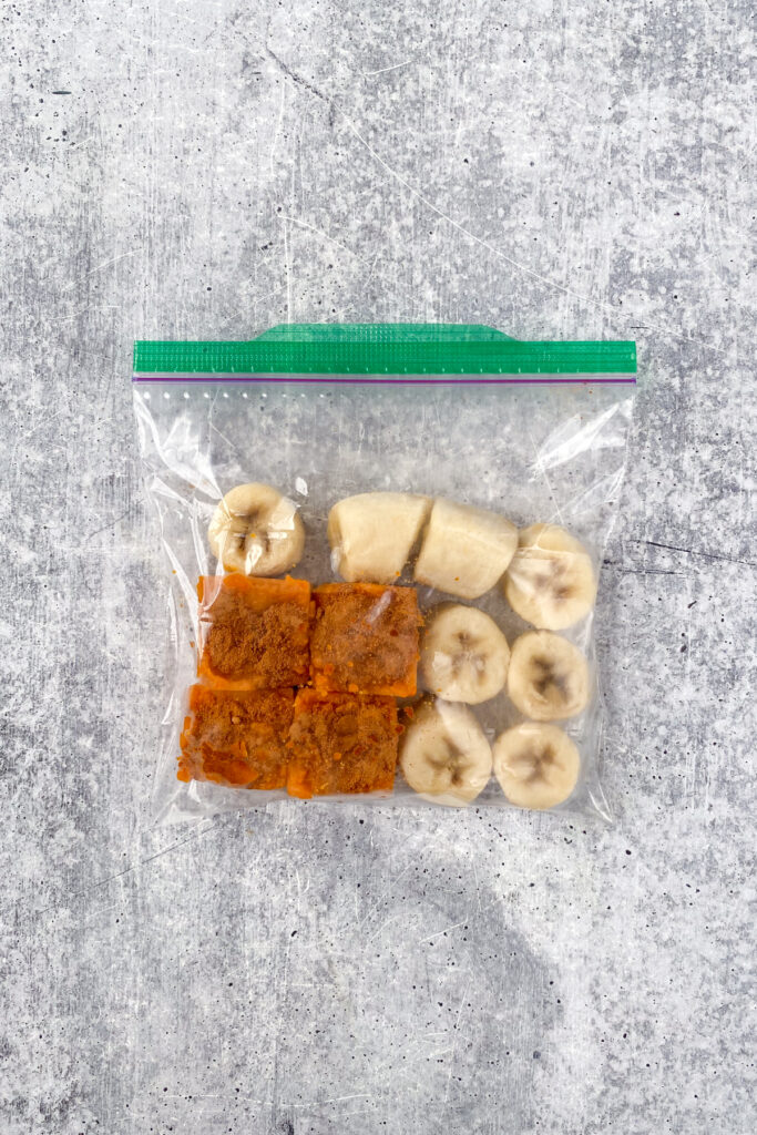 A homemade pumpkin smoothie freezer pack which is a small baggie containing for four frozen pumpkin cubes with pumpkin pie spice on top and a frozen banana that's been cut into eight chunks for easy blending.
