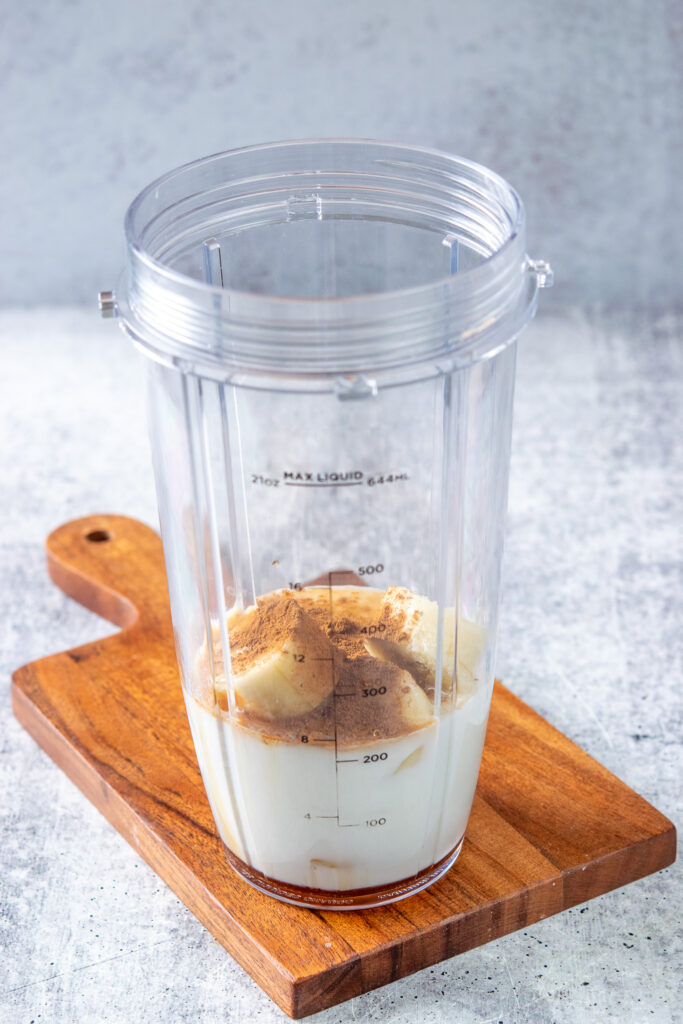 A blender cup with milk, frozen banana chunks and pumpkin pie spice.