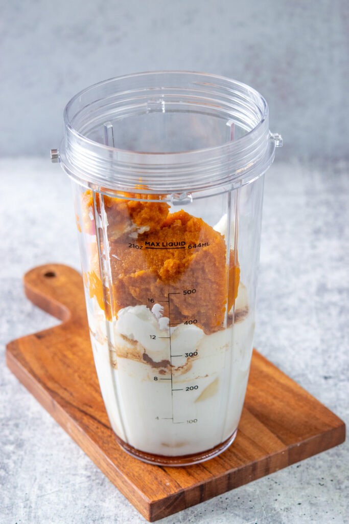 Pumpkin puree added on top of all the other ingredients in a blender cup to make a smoothie.