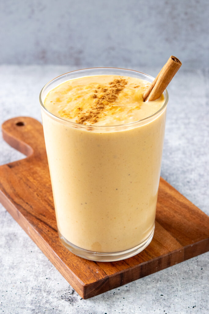 The pumpkin smoothie in a drinking glass garnished with cinnamon and a cinnamon stick.