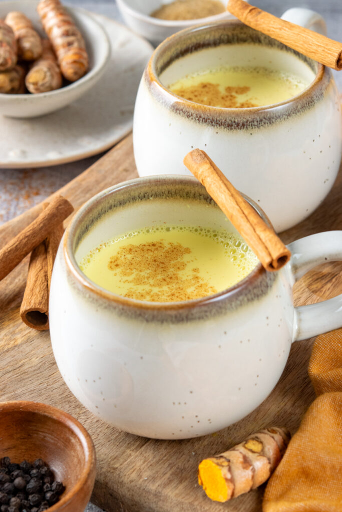 Two turmeric lattes in small mugs. Each golden milk latte is sprinkled with cinnamon and looks frothy and delicious.