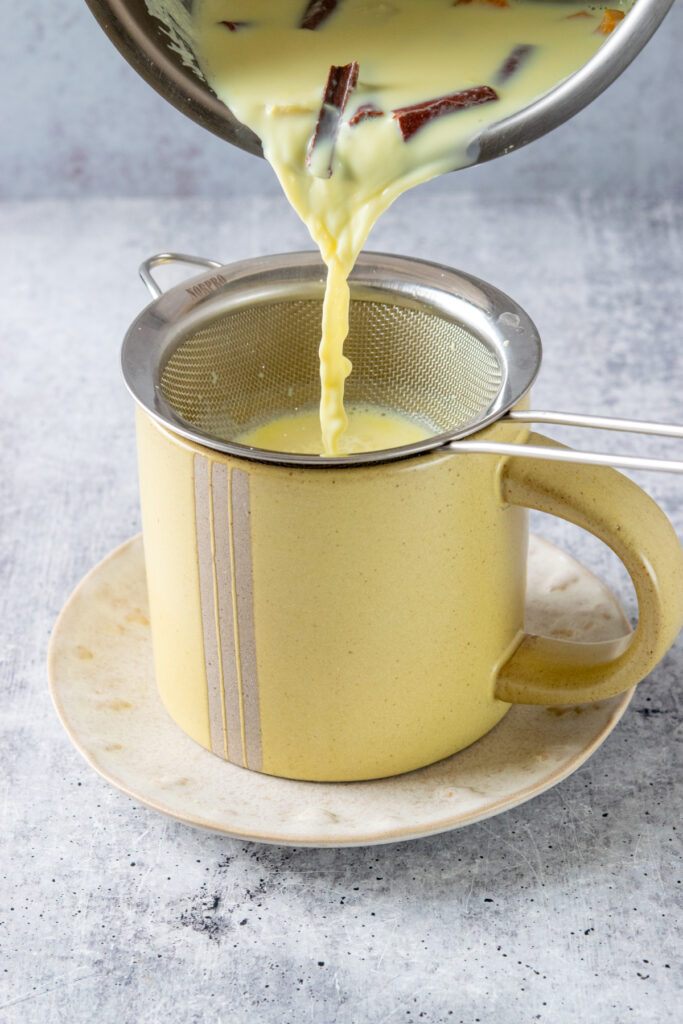 Pouring the turmeric latte through a strainer into a yellow mug.
