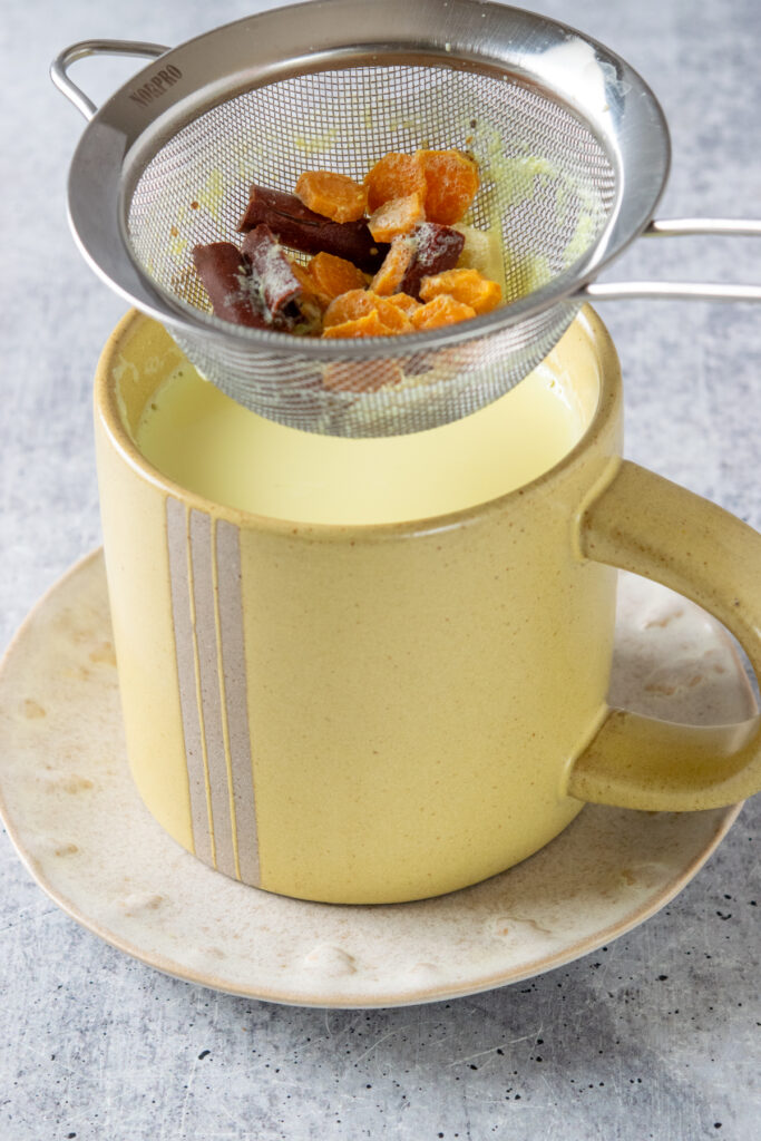 Lifting the strainer out of the mug. In the strainer you can see the sliced turmeric and ginger root, and cinnamon sticks.