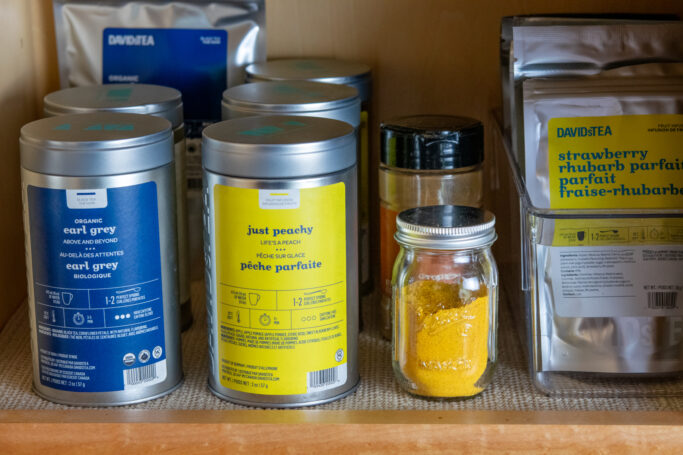 A small jar of homemade turmeric latte mix in my tea cabinet next to canisters of loose tea and a bottle of ground cinnamon.