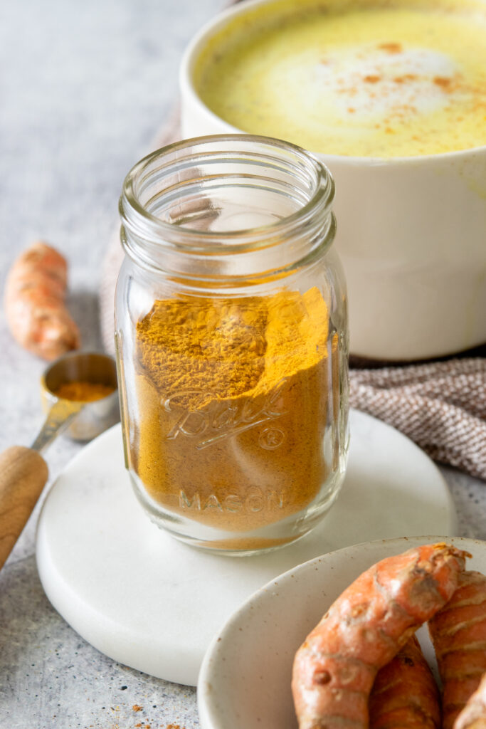 A bottle of golden-colored turmeric latte mix, next to a turmeric latte that has cinnamon sprinkled on top.