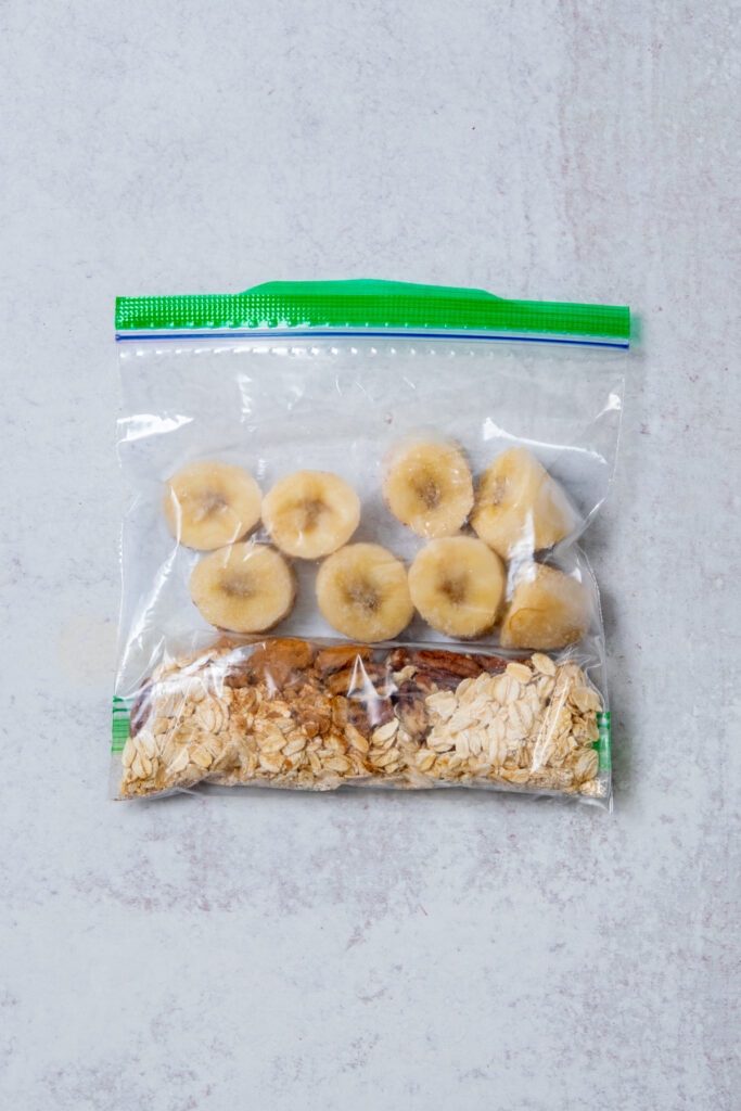 A homemade pecan oatmeal smoothie freezer pack that contains a small bag of oats, pecans, cinnamon and salt, and a frozen banana that's been cut into one-inch pieces.