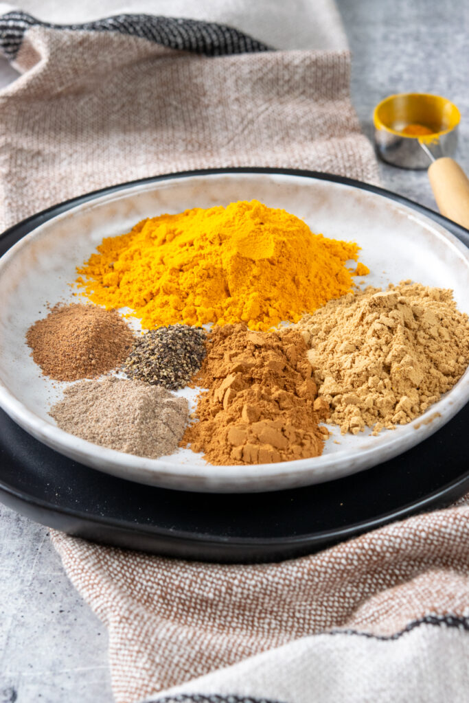 A plate with piles of the six ground spices that go into this blend of homemade turmeric latte mix.