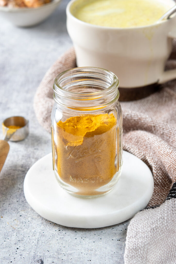 A jar of homemade turmeric latte mix in front of a golden turmeric latte that was made with the powder mix.