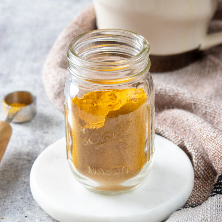 A jar of homemade turmeric latte mix in front of a golden turmeric latte that was made with the powder mix.
