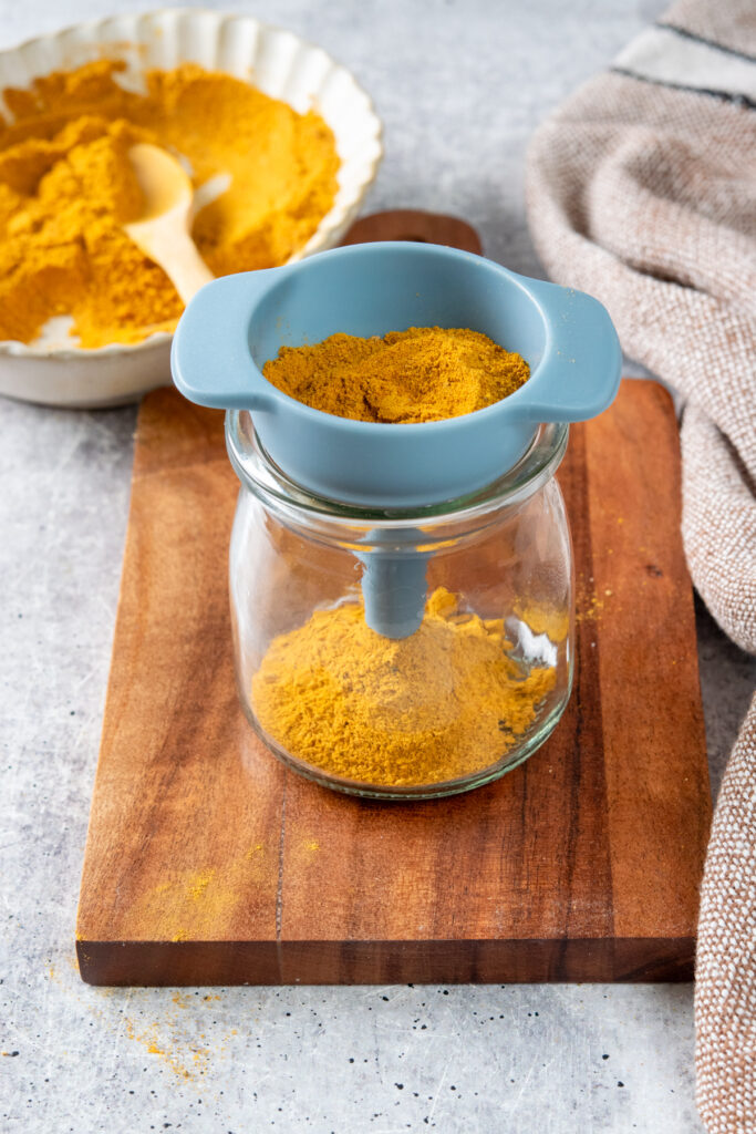 Putting the homemade turmeric latte mix into to small glass jar using a funnel.