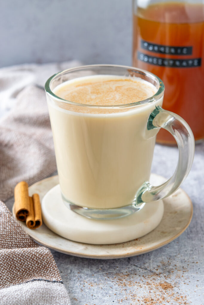 A golden milk turmeric tea latte topped with cinnamon powder next to a bottle of homemade turmeric tea concentrate.