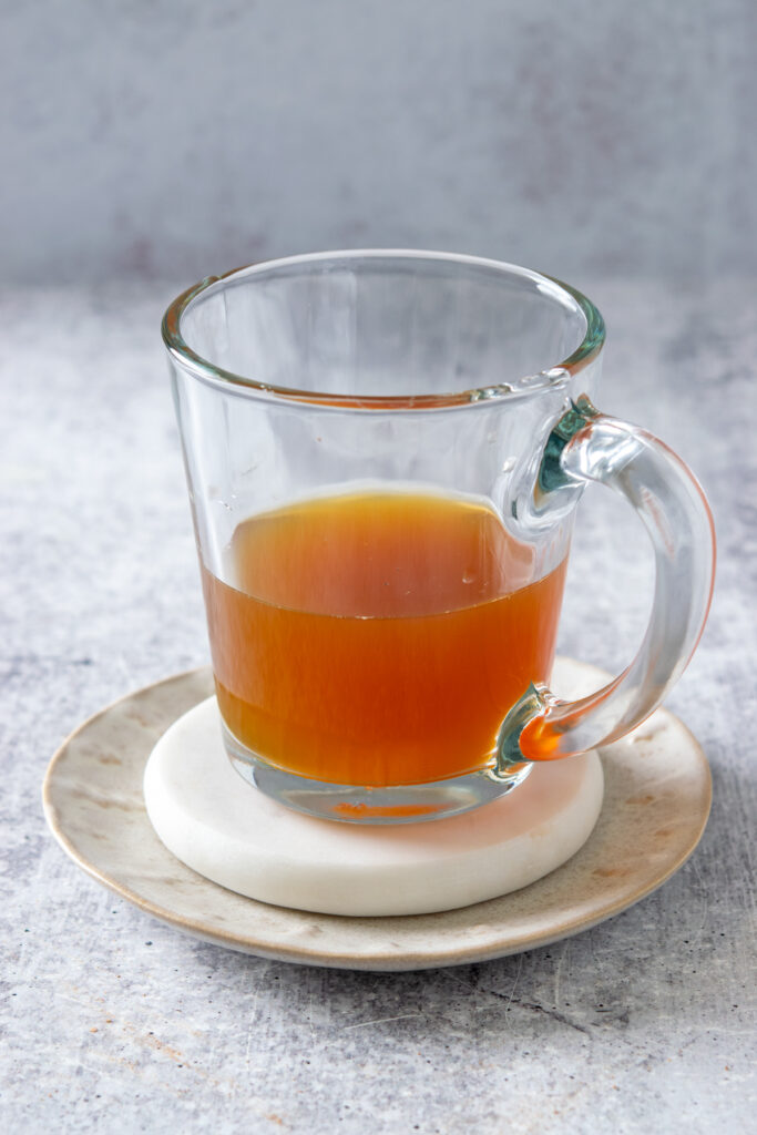 Showing a turmeric tea latte being made in a glass mug. The mug is filled halfway with homemade turmeric concentrate.