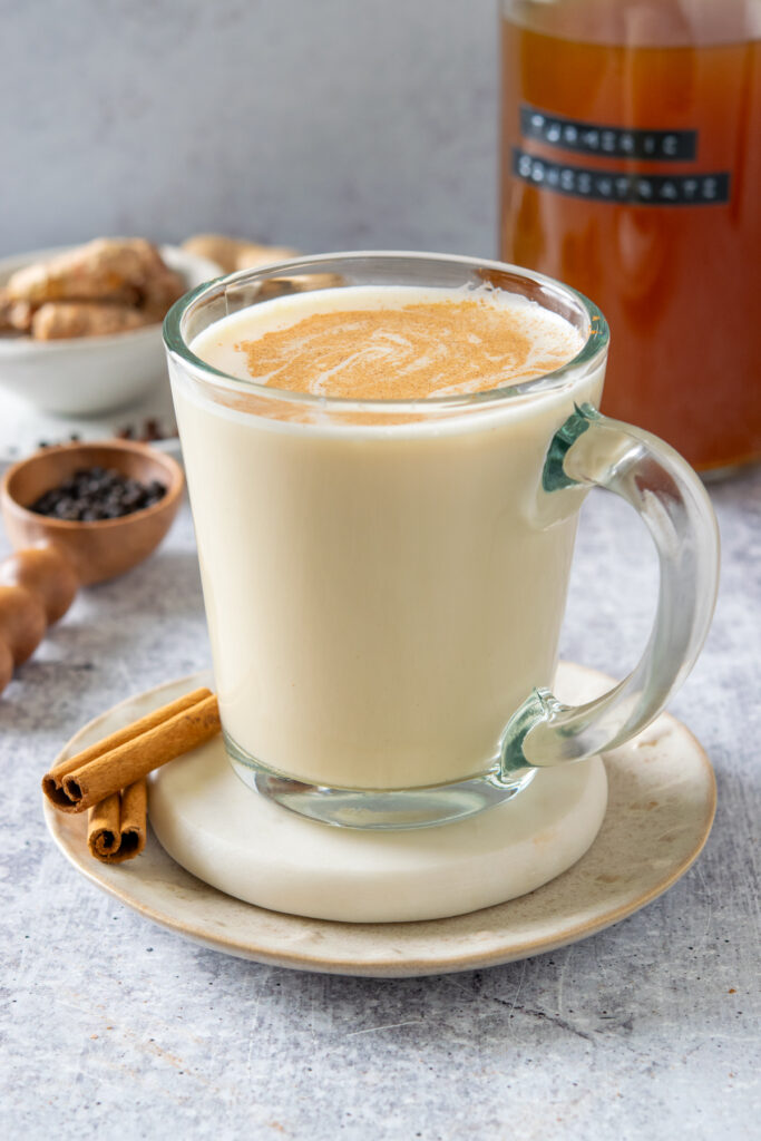 A turmeric latte with cinnamon sprinkled on top, which is next to a bottle of homemade turmeric concentrate.