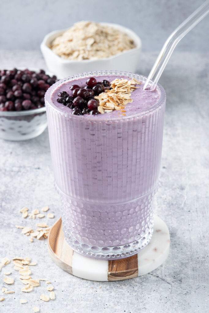 A wild blueberry oatmeal smoothie in a glass. The smoothie is purple with flecks of the blueberry in it.