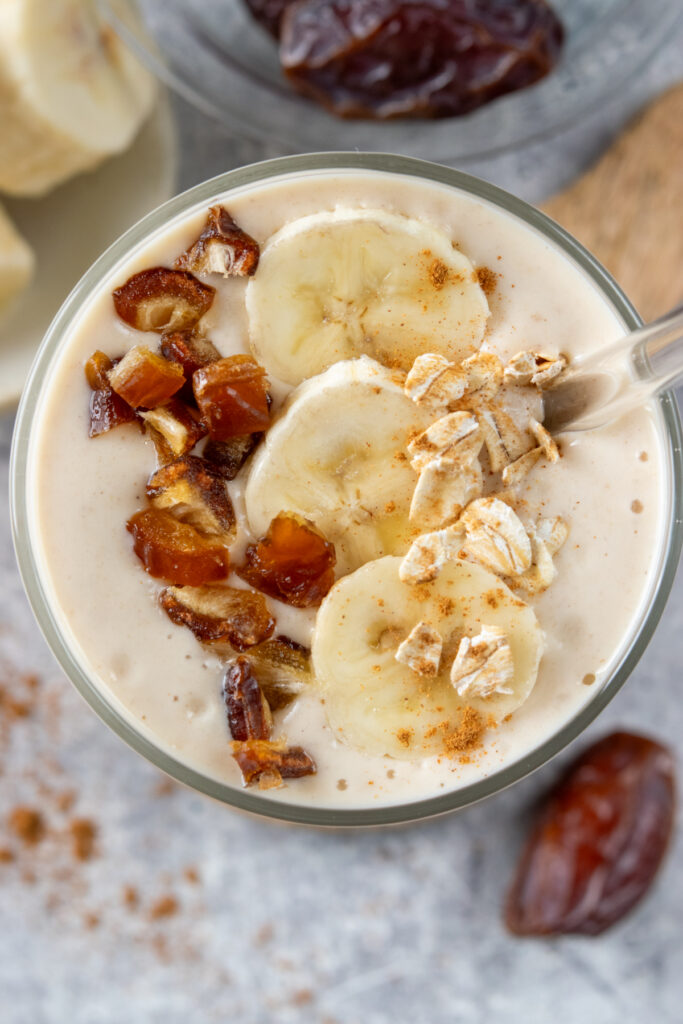 Medjool dates chopped on top of a banana date smoothie. There is also a bowl of dates and a single Medjool date next to the drink.