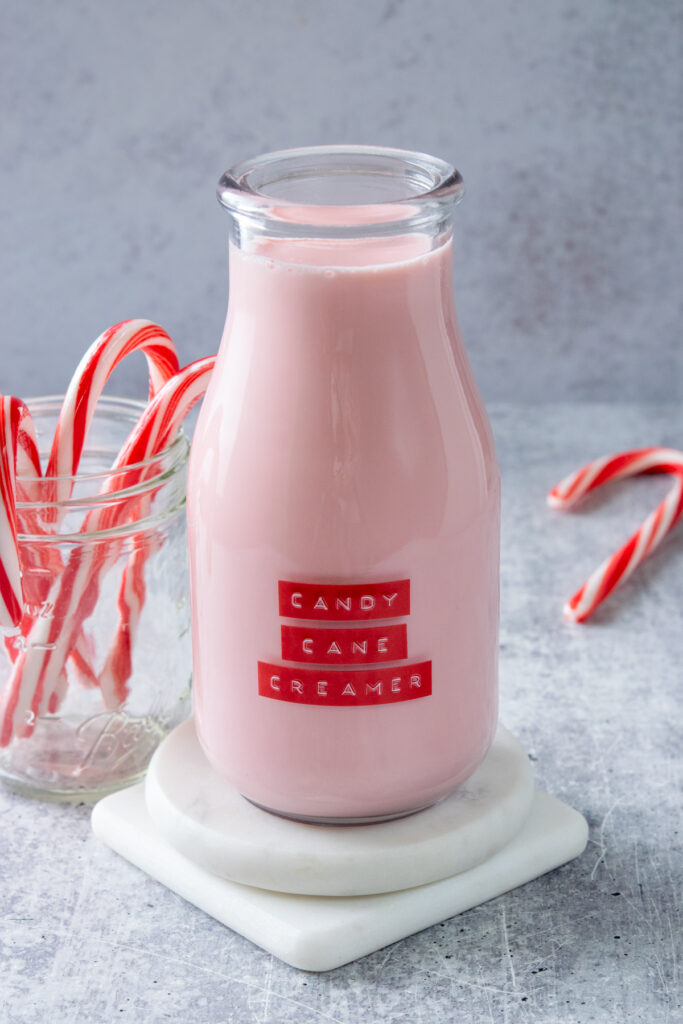 Homemade candy cane coffee creamer in a bottle next to a jar filled with candy canes.